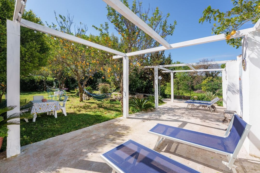 A spacious outdoor terrace with white pergolas, blue loungers, dining areas, and lush gardens under clear blue skies.