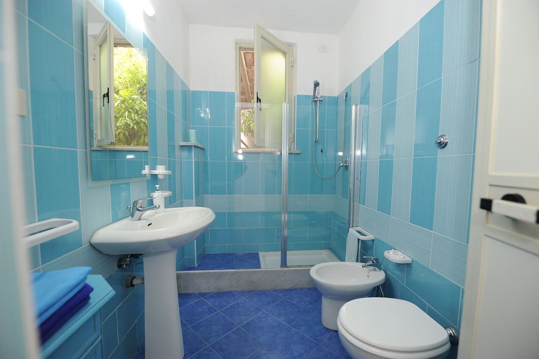 A bright blue-tiled bathroom featuring dual sinks, a shower enclosure, and natural light from windows.